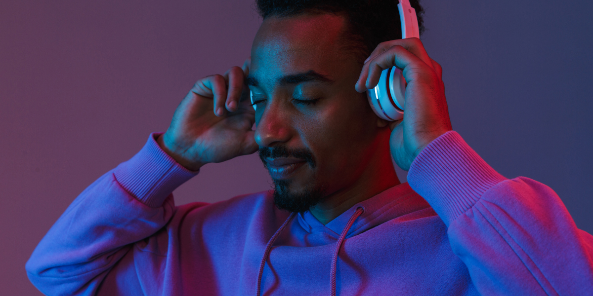A man bathed in purple light is closing his eyes as he puts on his headphones and listens to his music