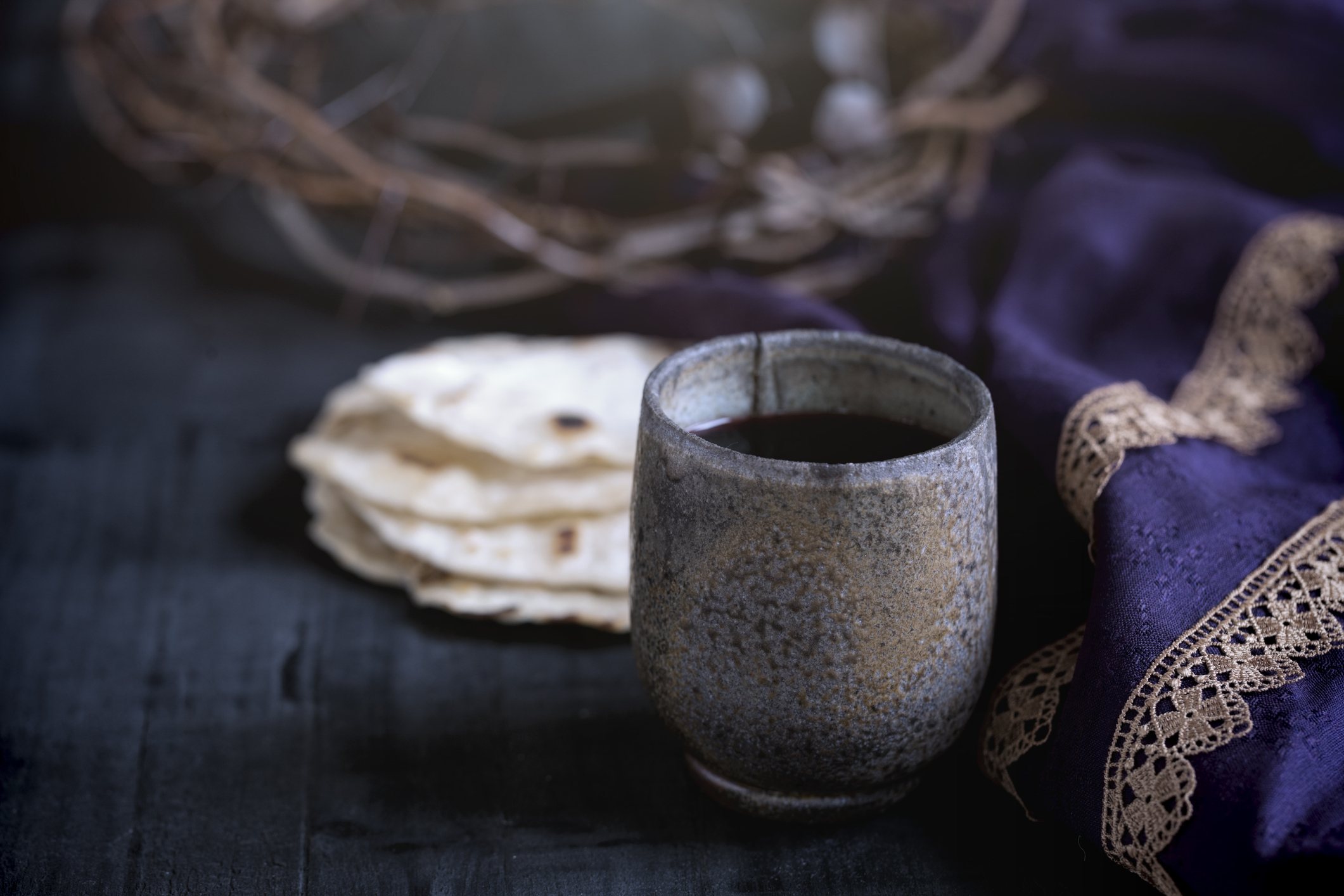 Easter crown of thorns with nails, royal purple robe, unleavened bread and a cup of wine on an old wood background with copy space.