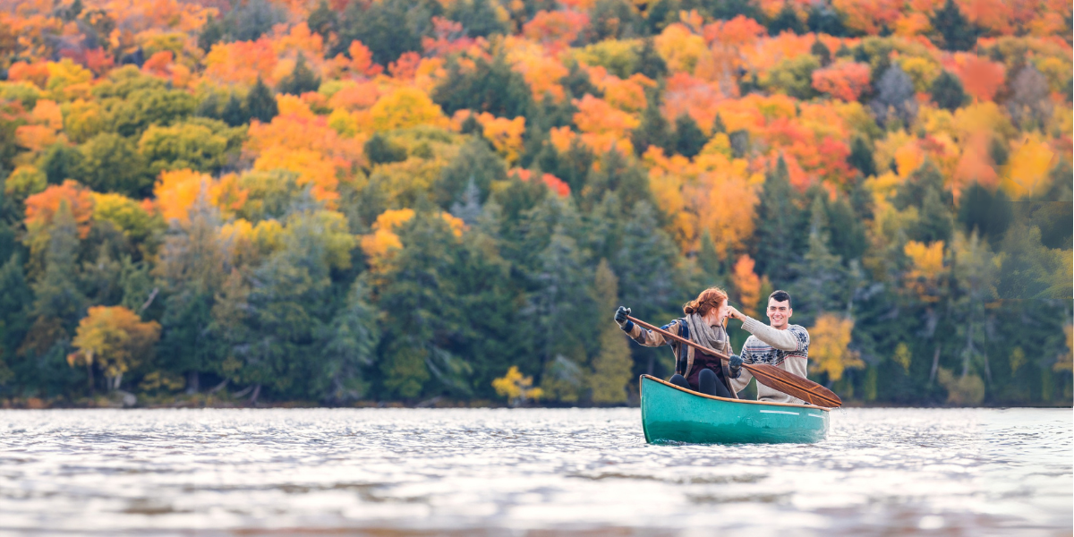 A couple on a lake canoeing together. The trees behind them are brilliant fall colors