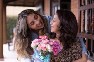 Loving daughter hugging mom from behind surprising her with flowers for motherâs day
