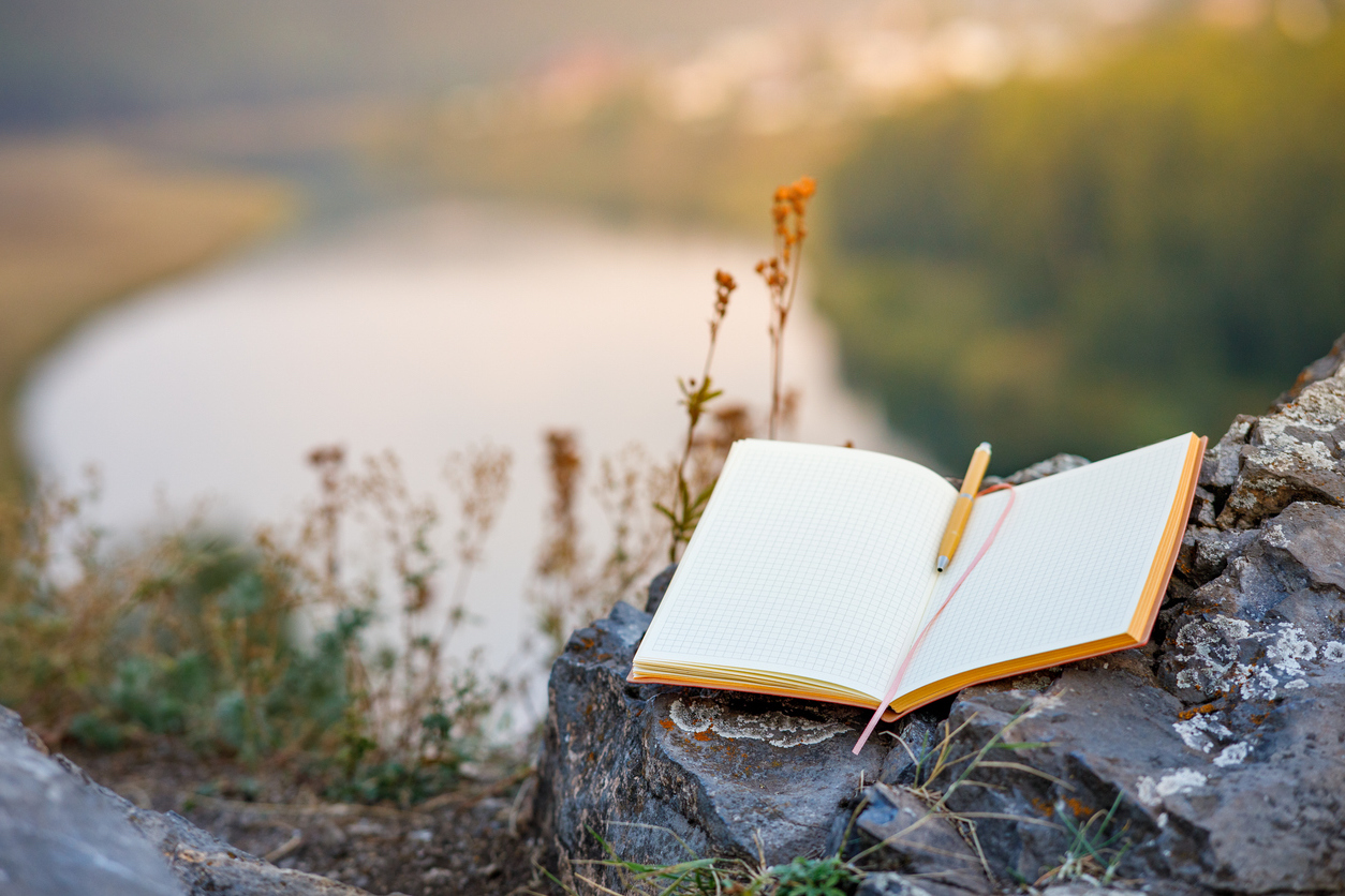 An open bullet journal sitting on a large stone out in nature.