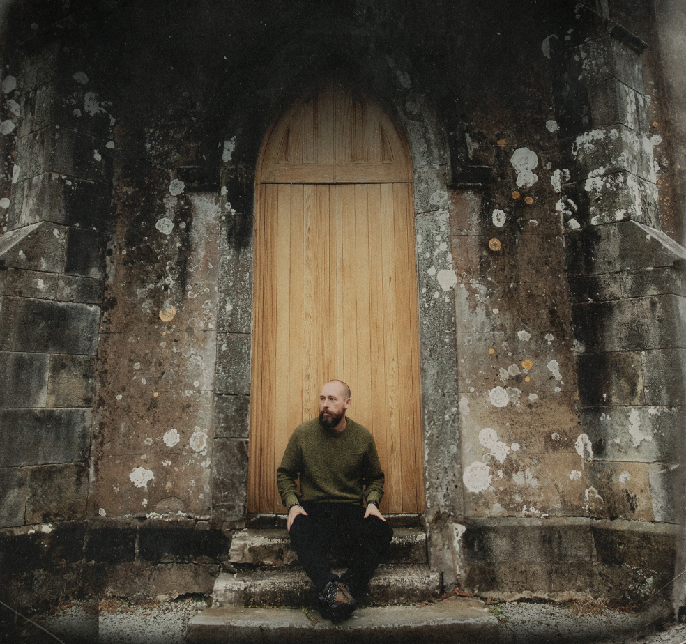 Darren Mulligan sitting at the doorway of an old irish stone building. Perhaps a church or a castle