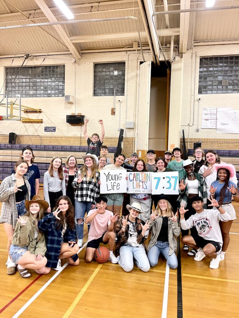 A large group of kids from Young Life in a gym holding up signs